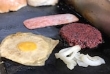 A fake egg, meat patty and bacon rasher on a frying pan.