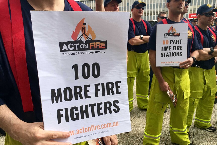 ACT firefighters protest outside the Legislative Assembly in Canberra. Close-up of sign reading "100 more fire fighters."