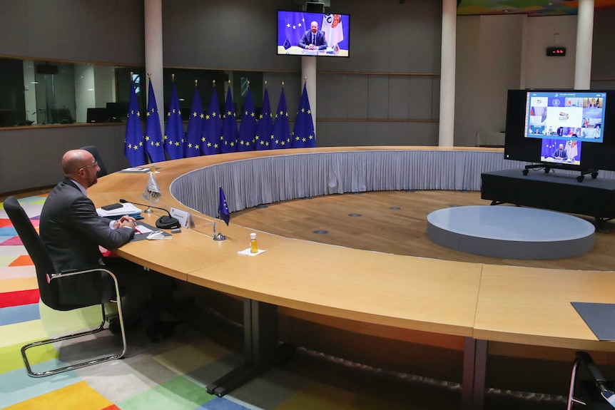European Council President Charles Michel sits alone at a large desk in front of a screen of G20 participants.