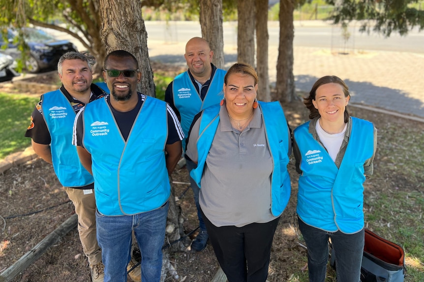 Five people standing under a tree wearing blue vests