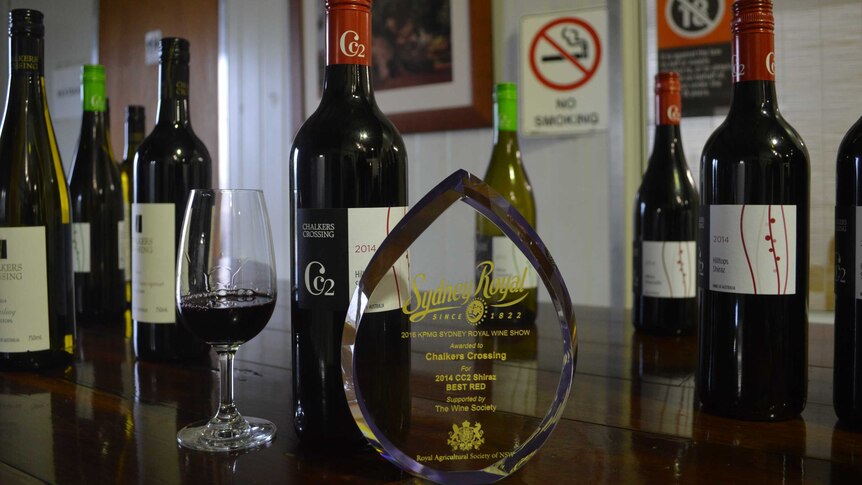 A glass trophy saying "Best Red", in front of a wine glass and bottle of the winning wine