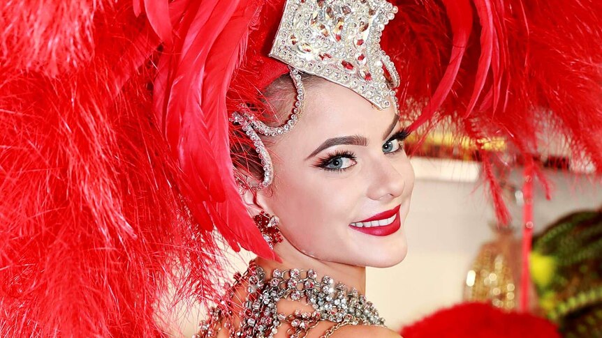 Dancer smiles into the camera, with an enormous red feather head dress.