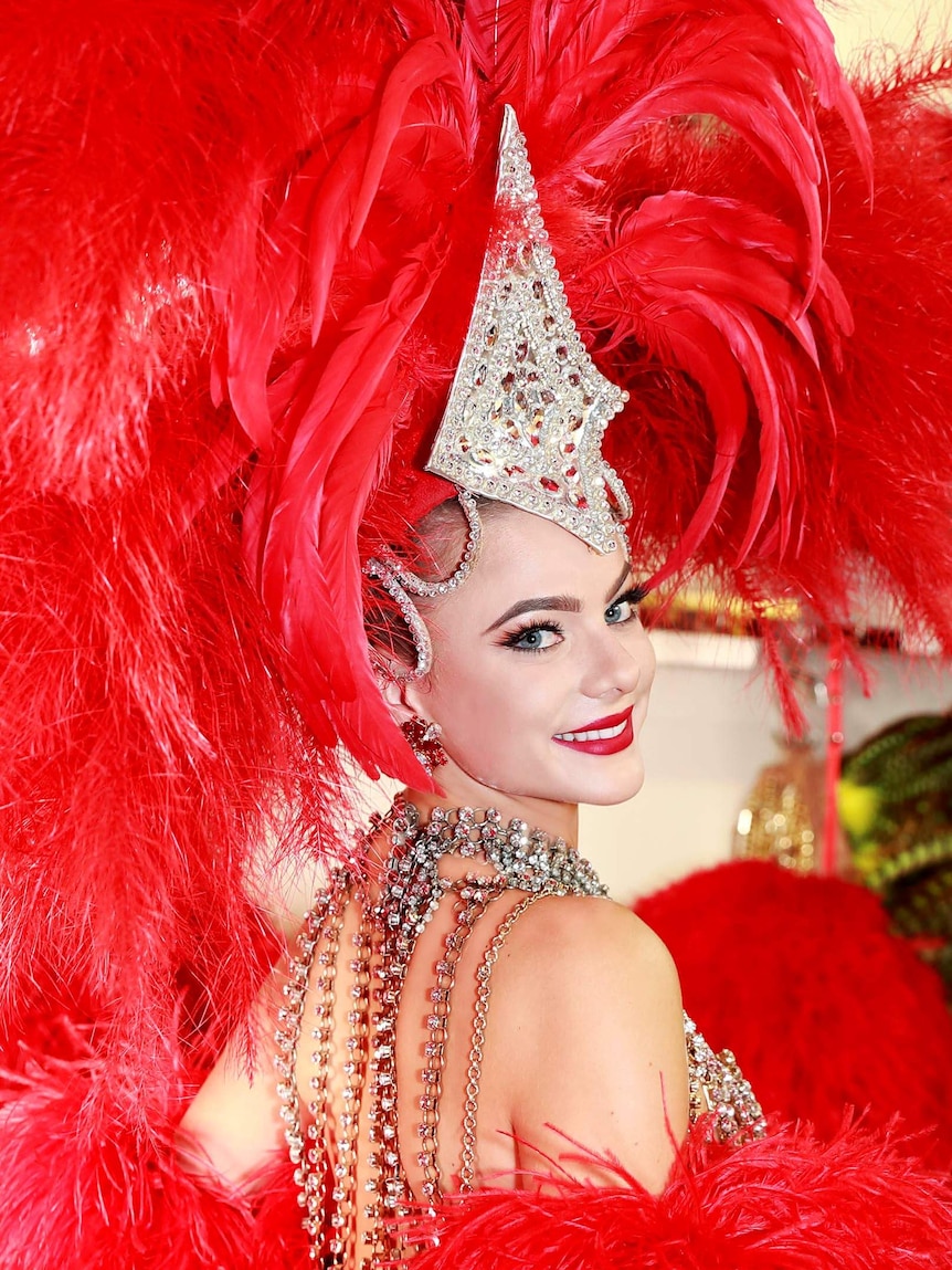 Dancer smiles into the camera, with an enormous red feather head dress.