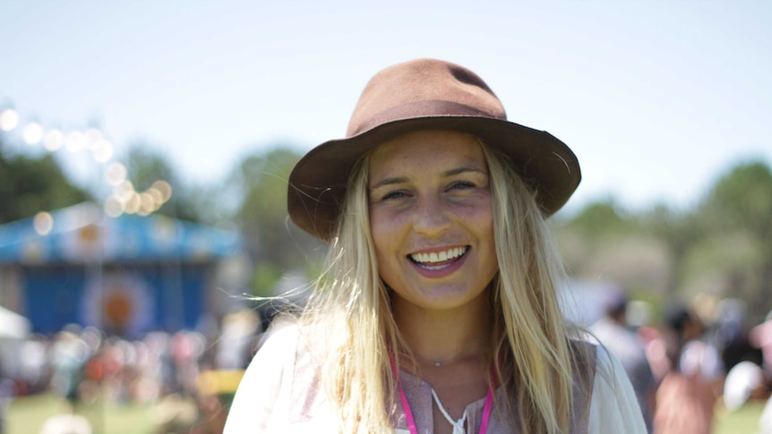 Portrait of a blonde woman wearing a broad hat, smiling at the camera, blurry backgroun.