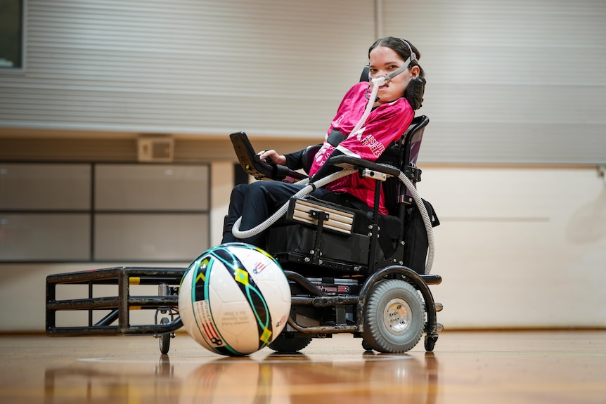 Rebecca Evans sitting on court in her powerchair with a football in the foreground.