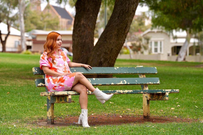 Red-haired woman wearing colourful dress sits on a park bench