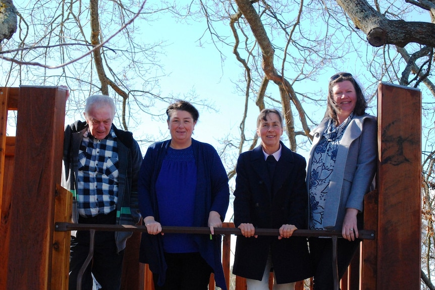 Four people stand atop of wooden play structure looking at the camera