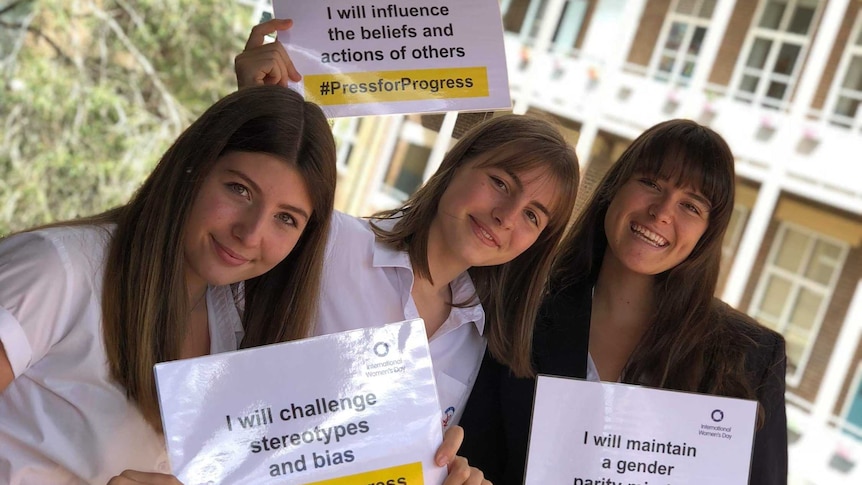 Three female high school students hold signs calling for equality.