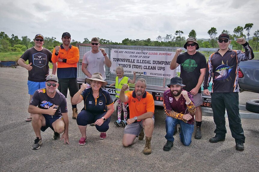 The group of 10 volunteers who form an illegal dumping clean-up group, stand in a semi-rural area in front of an empty trailer