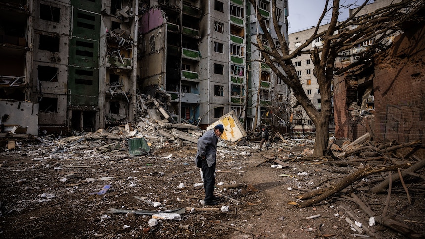 man stands in middle of rubble and broken buildings