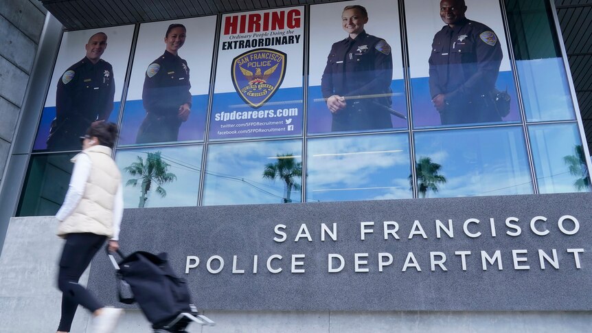 A woman walking past a building signed the San Francisco Police Department, with a recruitment banner above