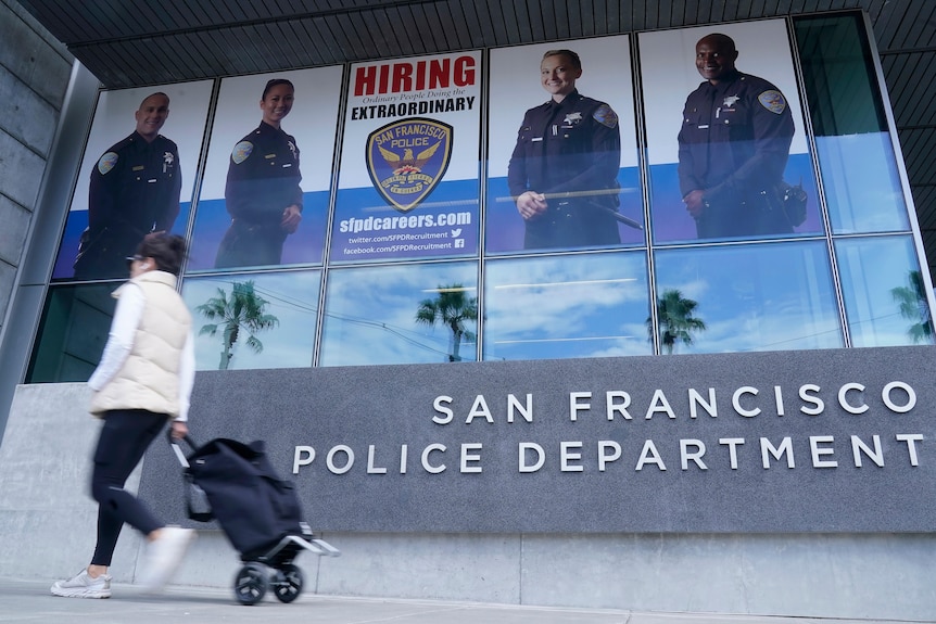 A woman walking past a building signed the San Francisco Police Department, with a recruitment banner above