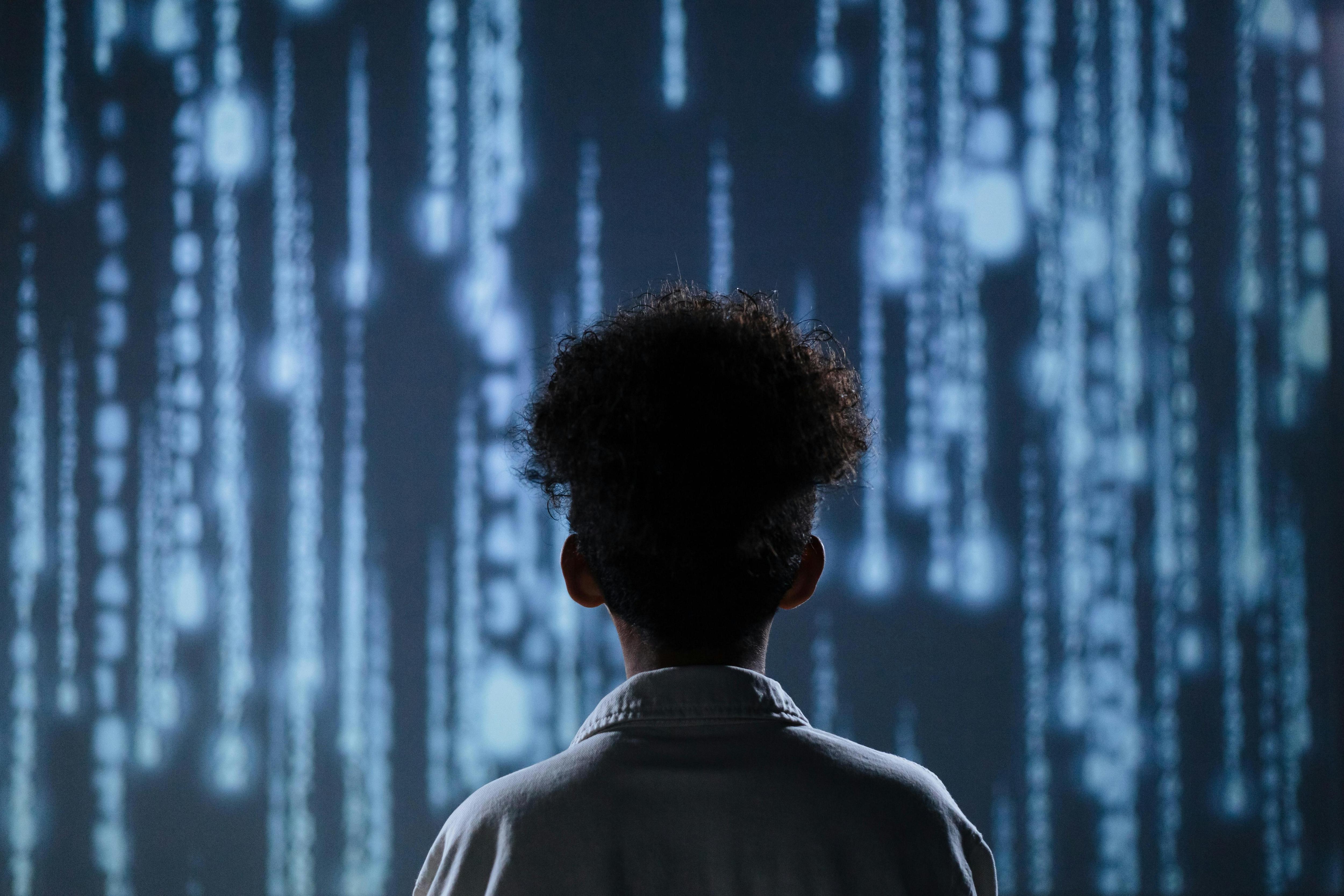 A teen boy stares at a digital background of code