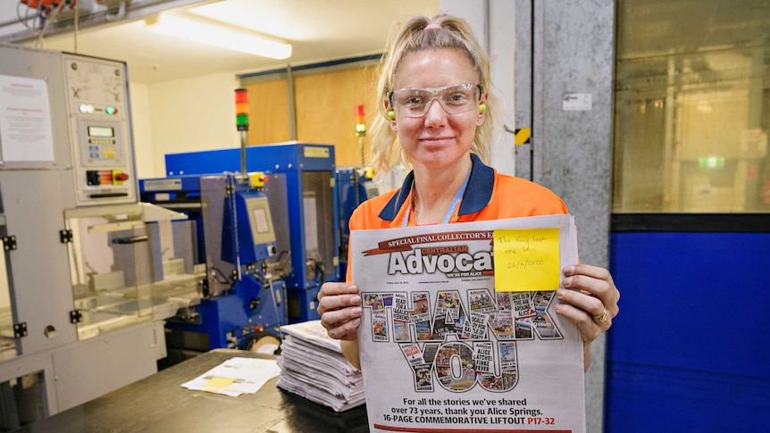 A female worker in an newspaper printing factory holds up a front page, printed with the words "thank you"