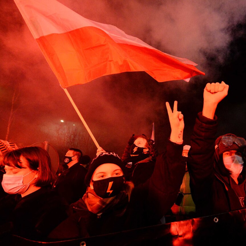 People dressed in warm clothes hold up their hands and flags in a night protest.