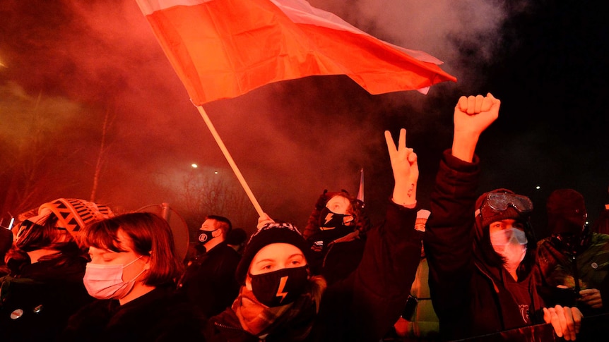 People dressed in warm clothes hold up their hands and flags in a night protest.