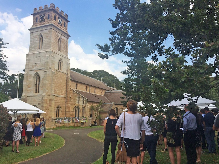 People gather outside a sandstone church.