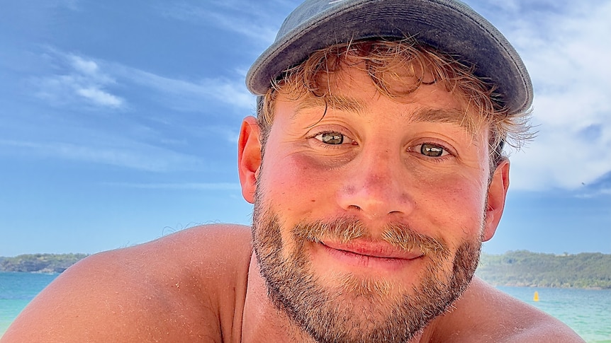 Influencer Tim Abbott takes a selfie while lying on the sand at the beach on a sunny day.
