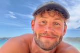 Influencer Tim Abbott takes a selfie while lying on the sand at the beach on a sunny day.