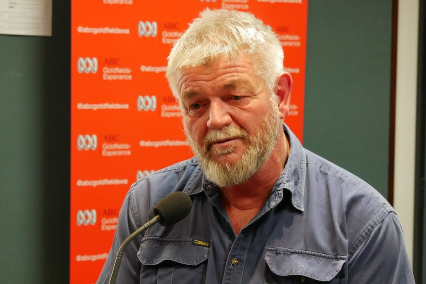 A man with silver hair and beard speaking into a microphone in an ABC studio.  