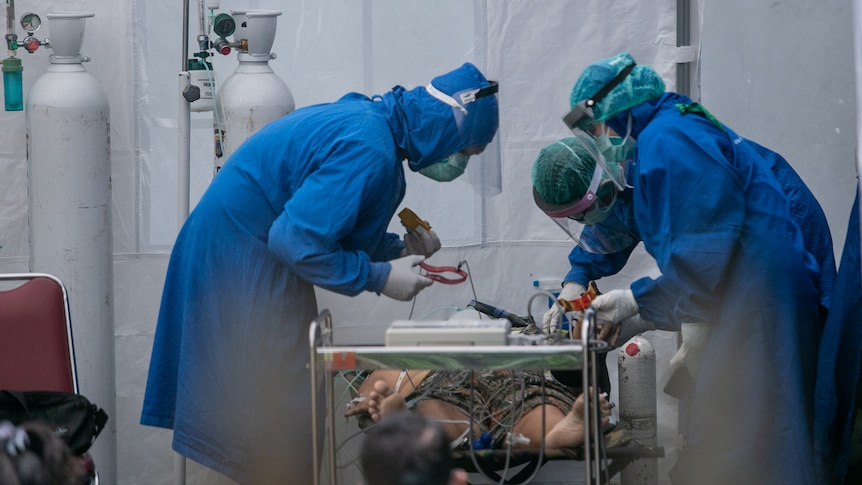 Several hospital staff in full PPE treat a patient on oxygen in a temporary care tent. 