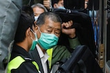 A man, surrounded by poice and supporters, enters a prison van, wearing a suit and face mask
