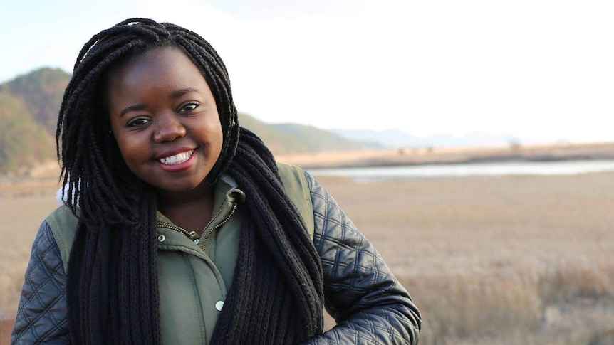 Lorraine Ngwenya smiles and leans against a wooden post.