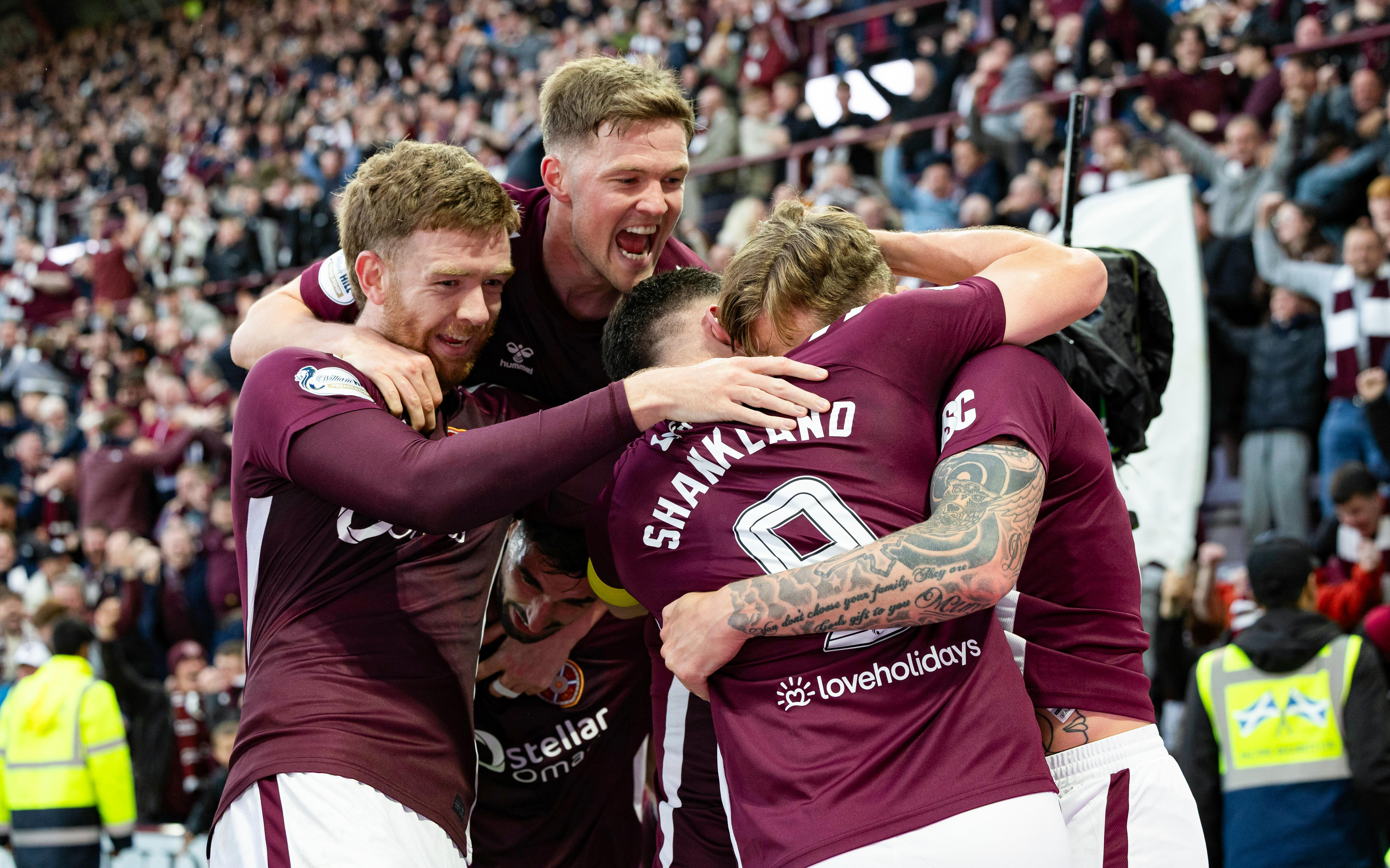 Four soccer players embrace after a goal, in front of cheering fans