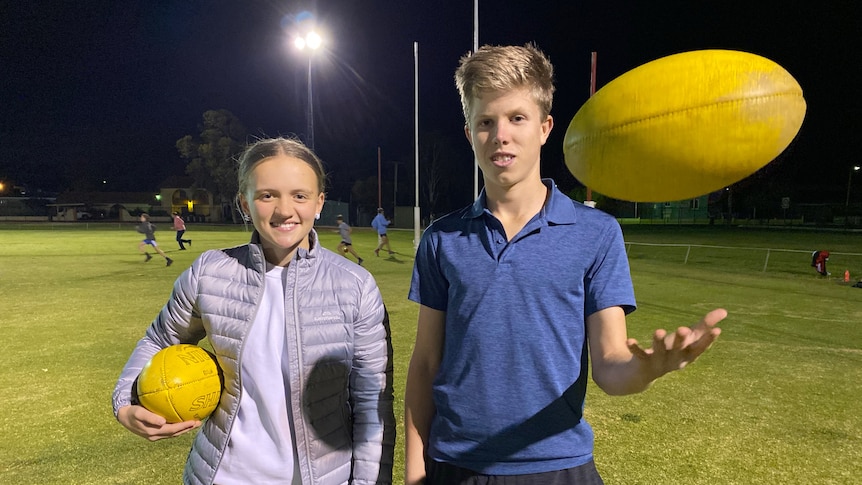 A girls holding a football and a boy throwing a football in the air stand next to each other. 