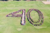 A large group of young people dressed in maroon, grey and white standing together to form the number 40 on a school oval.
