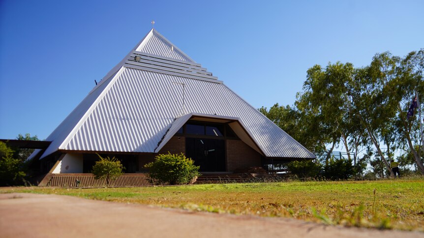A council building with a tall, white, pyramid-shaped roof, next to a patch of grass and trees.