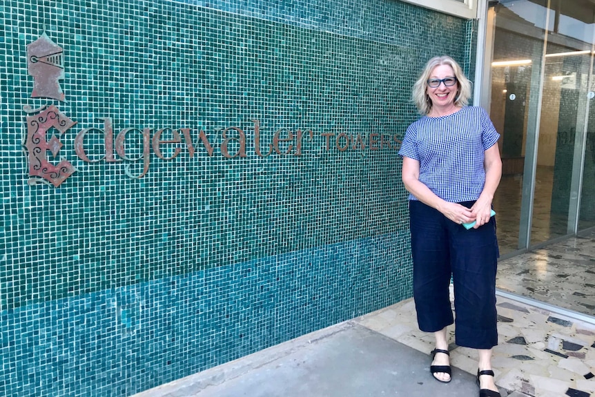 Di Kilsby stands outside her building with a sign saying Edgewater Towers.