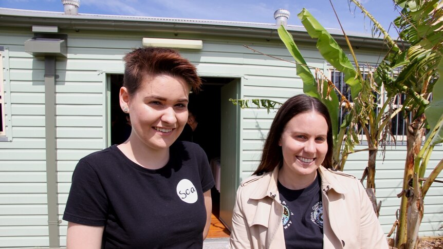 Two young women, Jamira Pemberton and Alyssa Kellam, standing in front of the Coomaditichie community hall