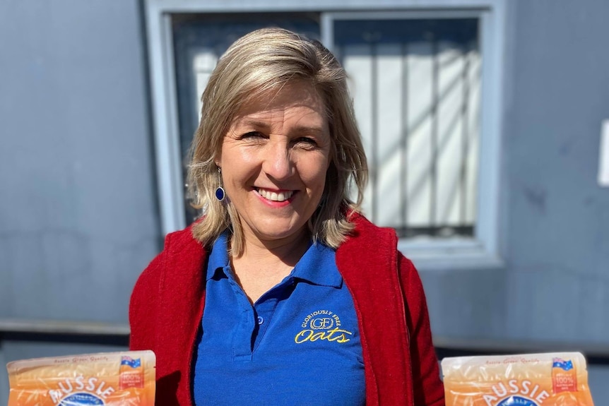 A lady smiling at the camera holding two bags of oats. 