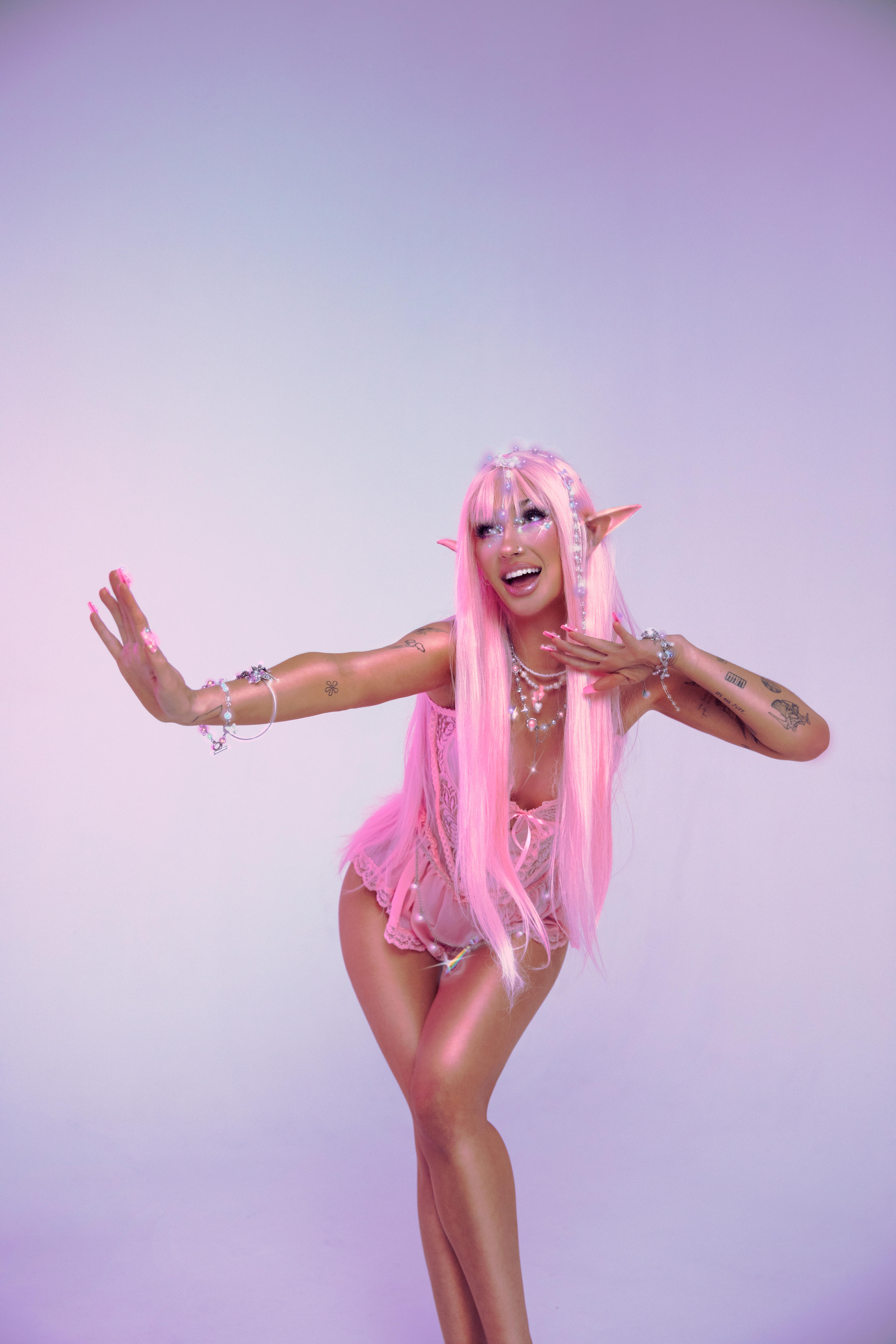 A portrait photo of Peach PRC in her pink fairy costuming and wings, leaning forward and smiling with an arm extended