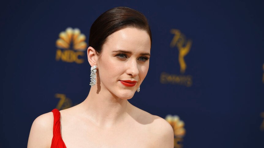 A woman wearing her hair in a bun, with dangling diamond earrings and a one-shouldered red dress