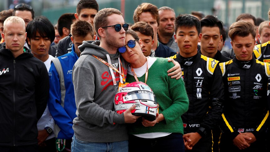 Anthoine Hubert's brother and mother hold the late driver's helmet and each other in front of sombre looking drivers
