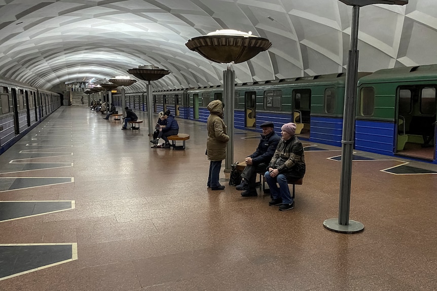 People sit at a metro station next to stopped trains.