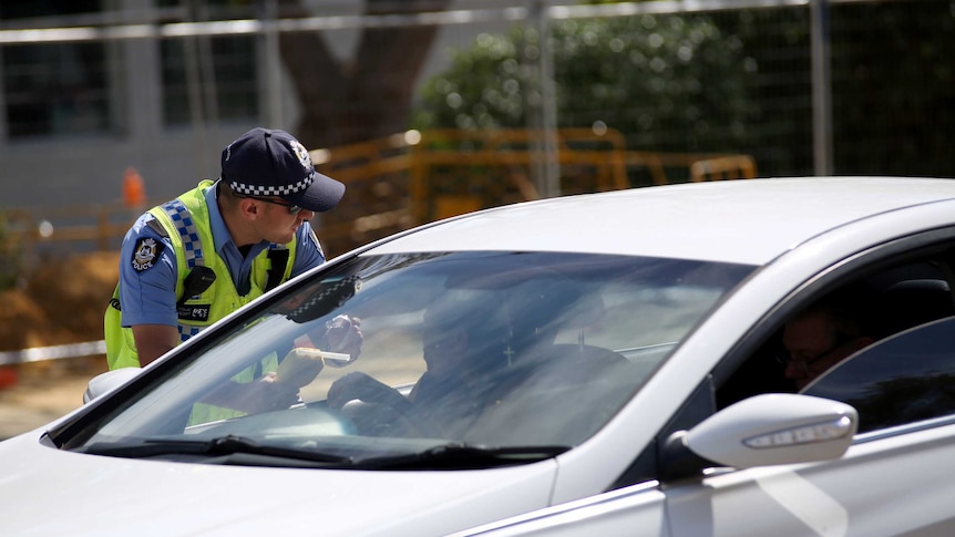 A policeman leans into the window of a car holding a breathalyser.