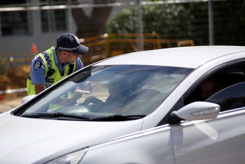 A policeman leans into the window of a car holding a breathalyser.