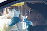 A woman sitting in a car has a swab placed in her nose by a person in protective gear