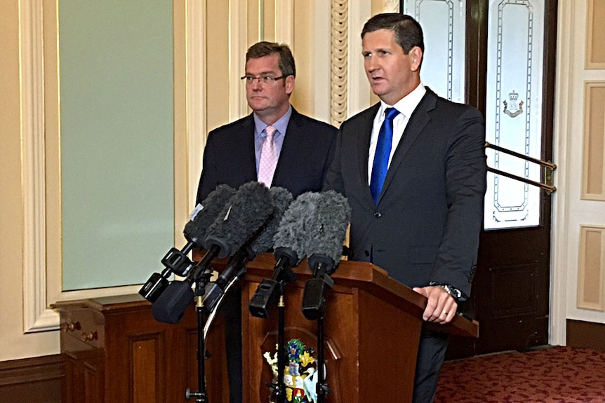 Lawrence Springborg speaks at a podium as John McVeigh stands next to him.
