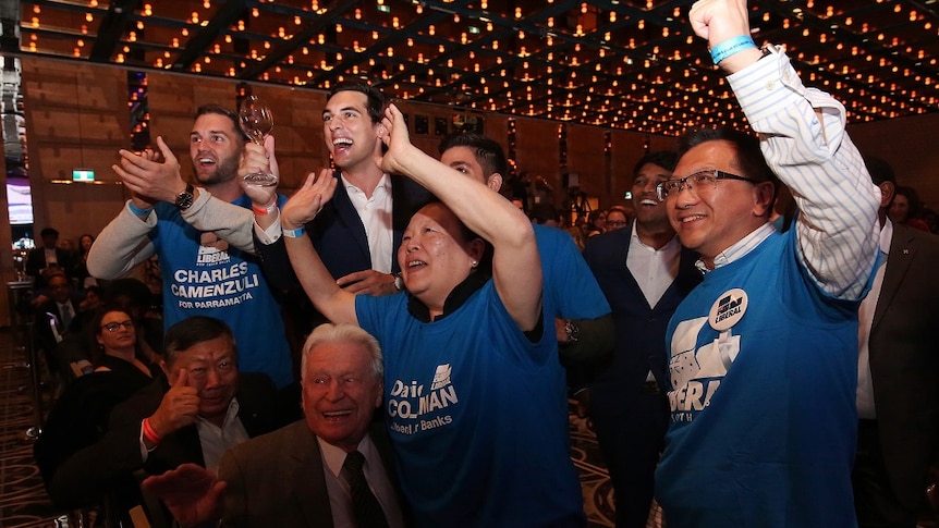 A group of politcal party supporters smile and cheer at a party function in a glitzy ballroom