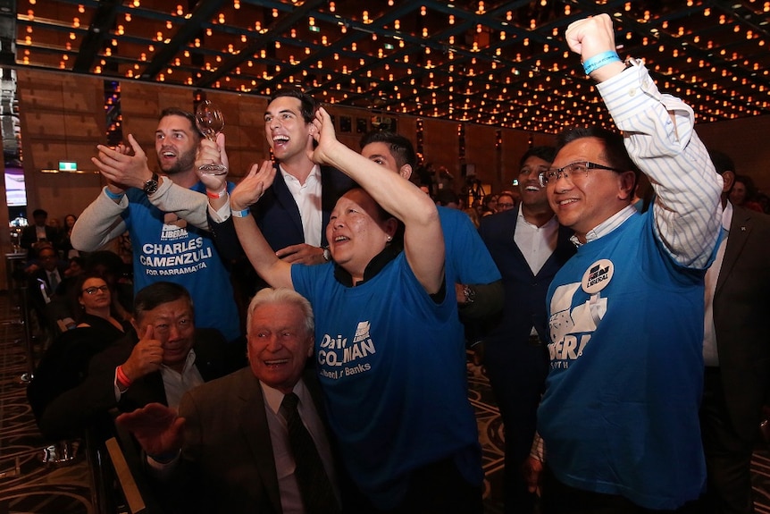 A group of politcal party supporters smile and cheer at a party function in a glitzy ballroom