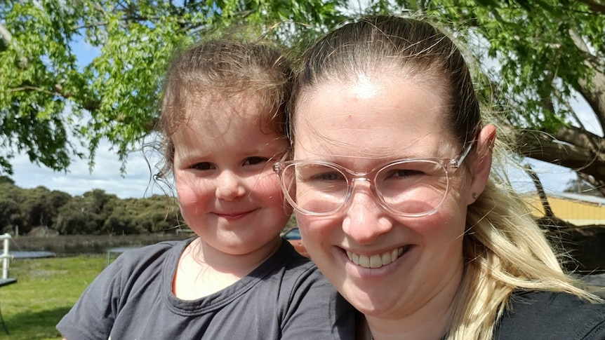 A woman and her young daughter take a self portrait on a park bench with trees behind