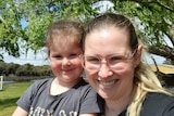 A woman and her young daughter take a self portrait on a park bench with trees behind