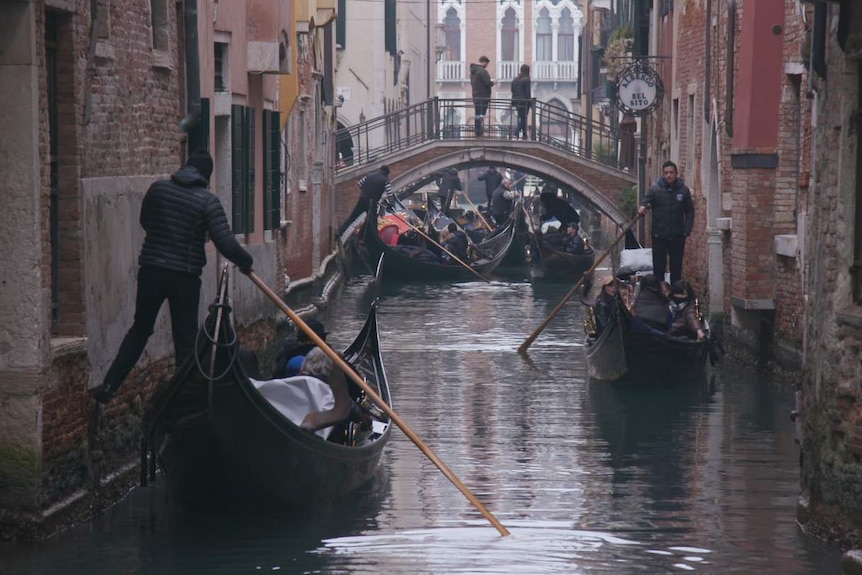 Gondolas navigate through a narrow passage in Venice.