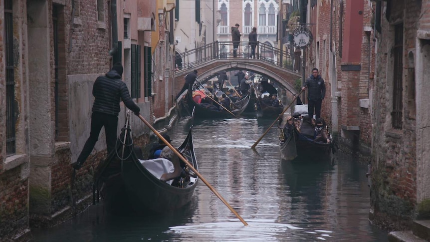 Gondolas navigate through a narrow passage in Venice.