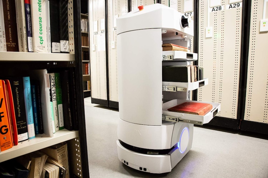 A robo-courier is carrying three shelves of books around library stacks.