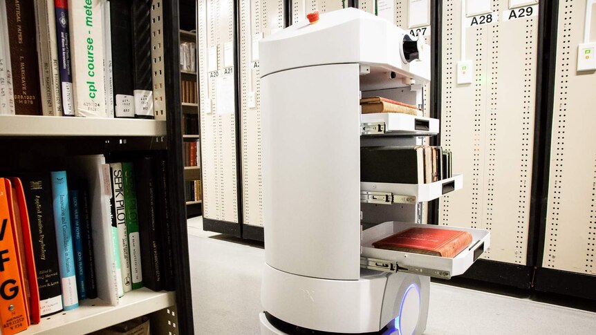 A robo-courier is carrying three shelves of books around library stacks.